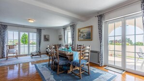 Un coin repas avec une table et des chaises en bois, un tapis à motifs et de grandes fenêtres avec des rideaux.