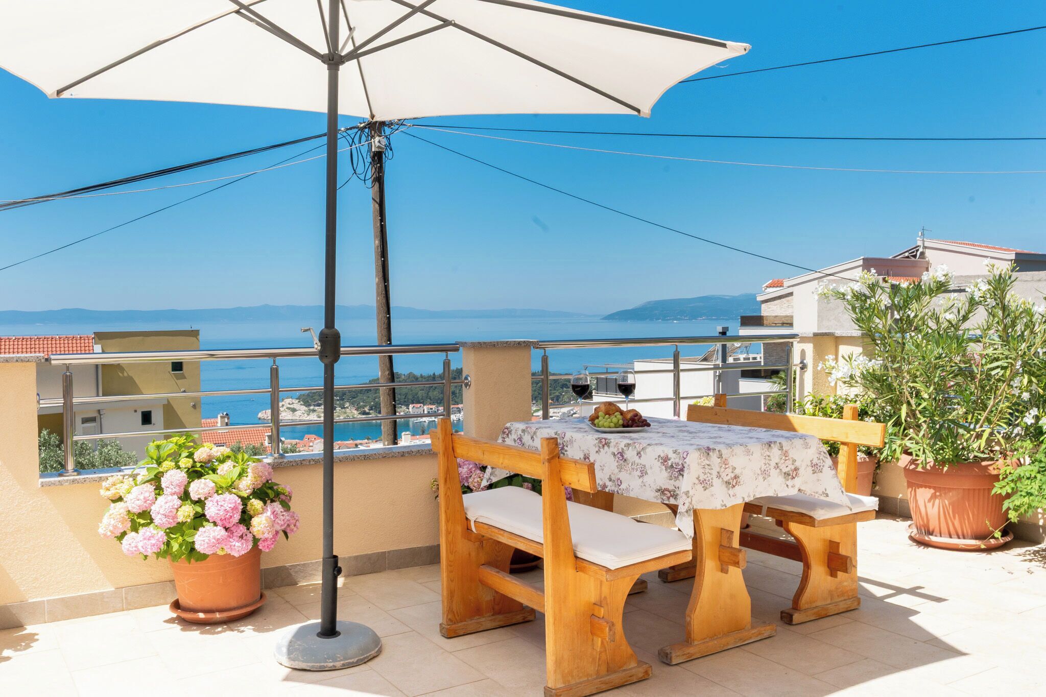 A balcony with a table, chairs, a potted plant, and a view of the sea.