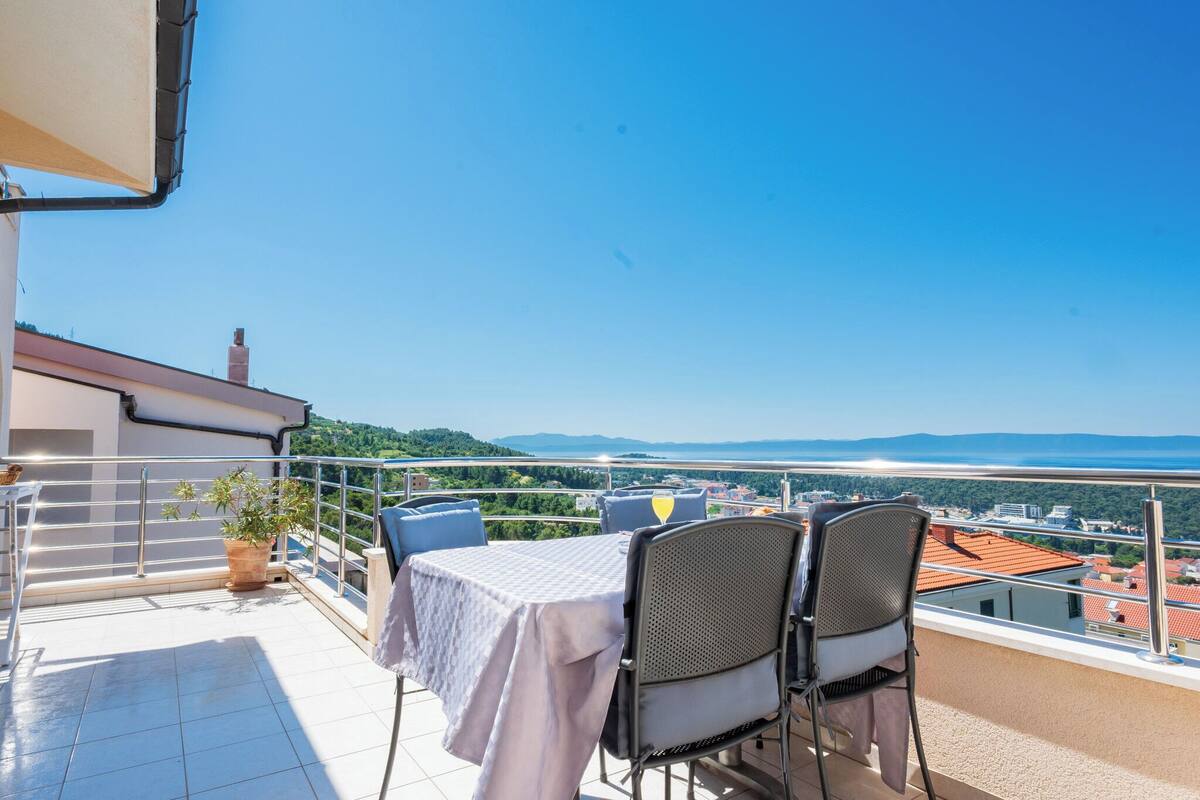 A balcony with a table and chairs, a potted plant, and a view of the city and hills.