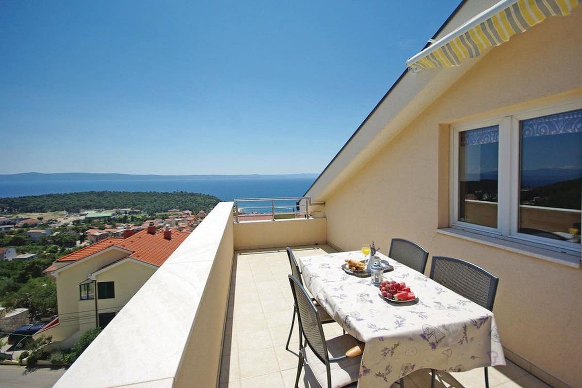 A balcony with a table set for two, overlooking a coastal view.