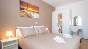 A bedroom with a bed, nightstand, lamp, artwork, wardrobe, desk, chair, and a mirror. - Apartments Pavlinovic (Makarska)