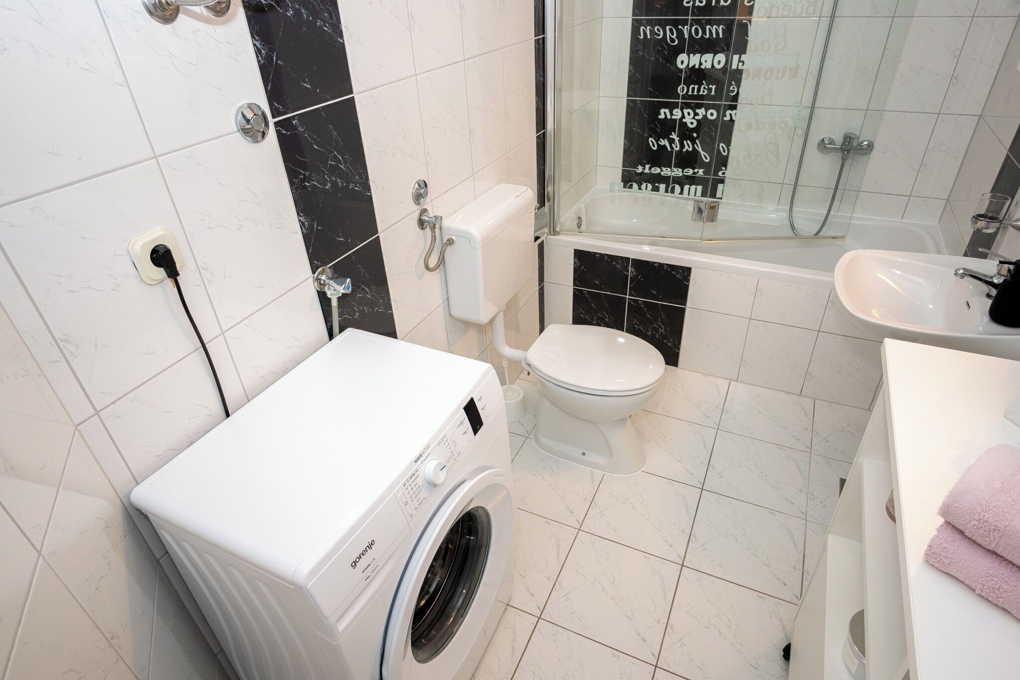 Une salle de bain équipée d’un lave-linge, de toilettes, d’une baignoire et d’un lavabo.