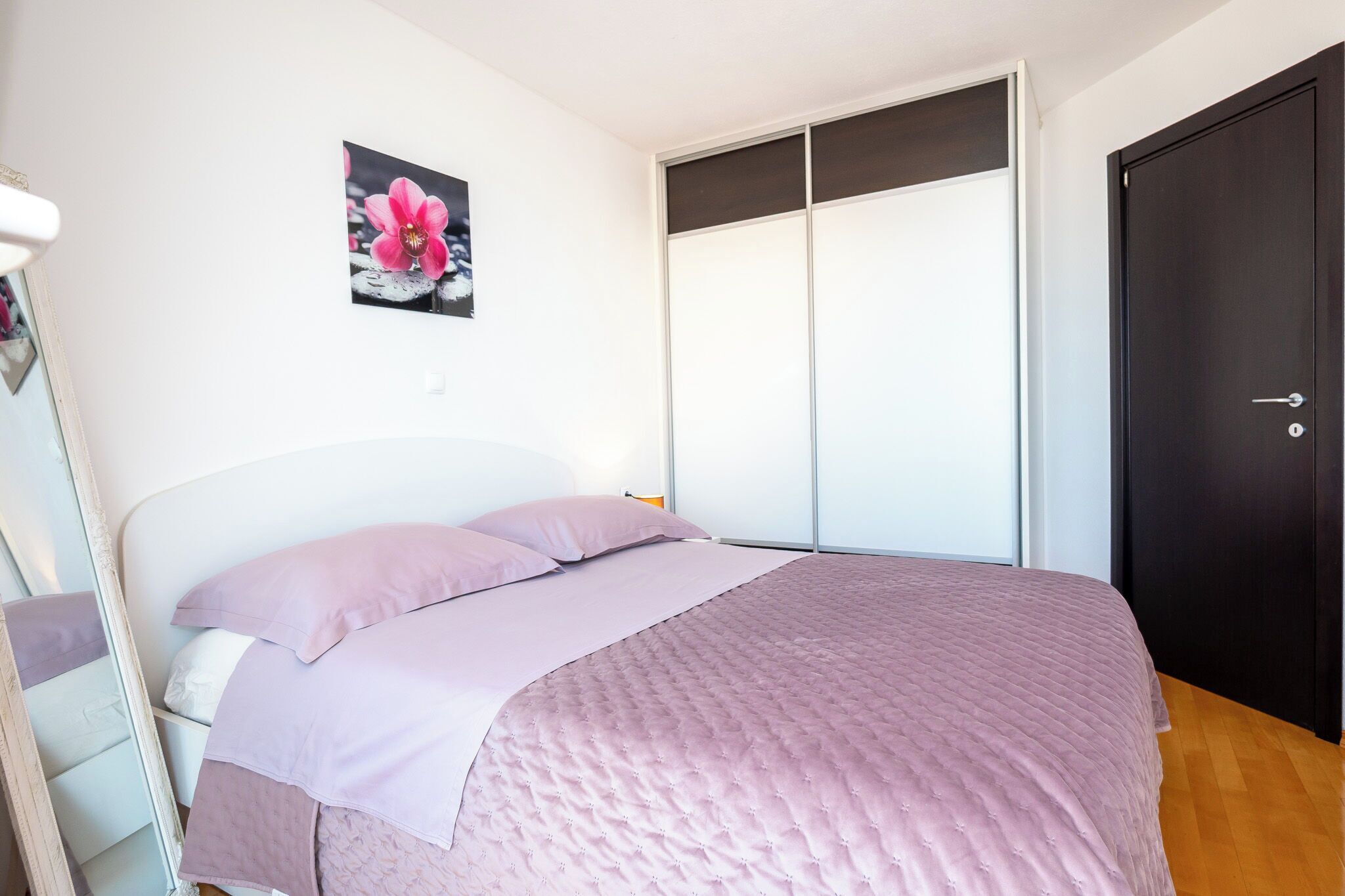A bedroom with a bed, a door, and a wall-mounted picture.