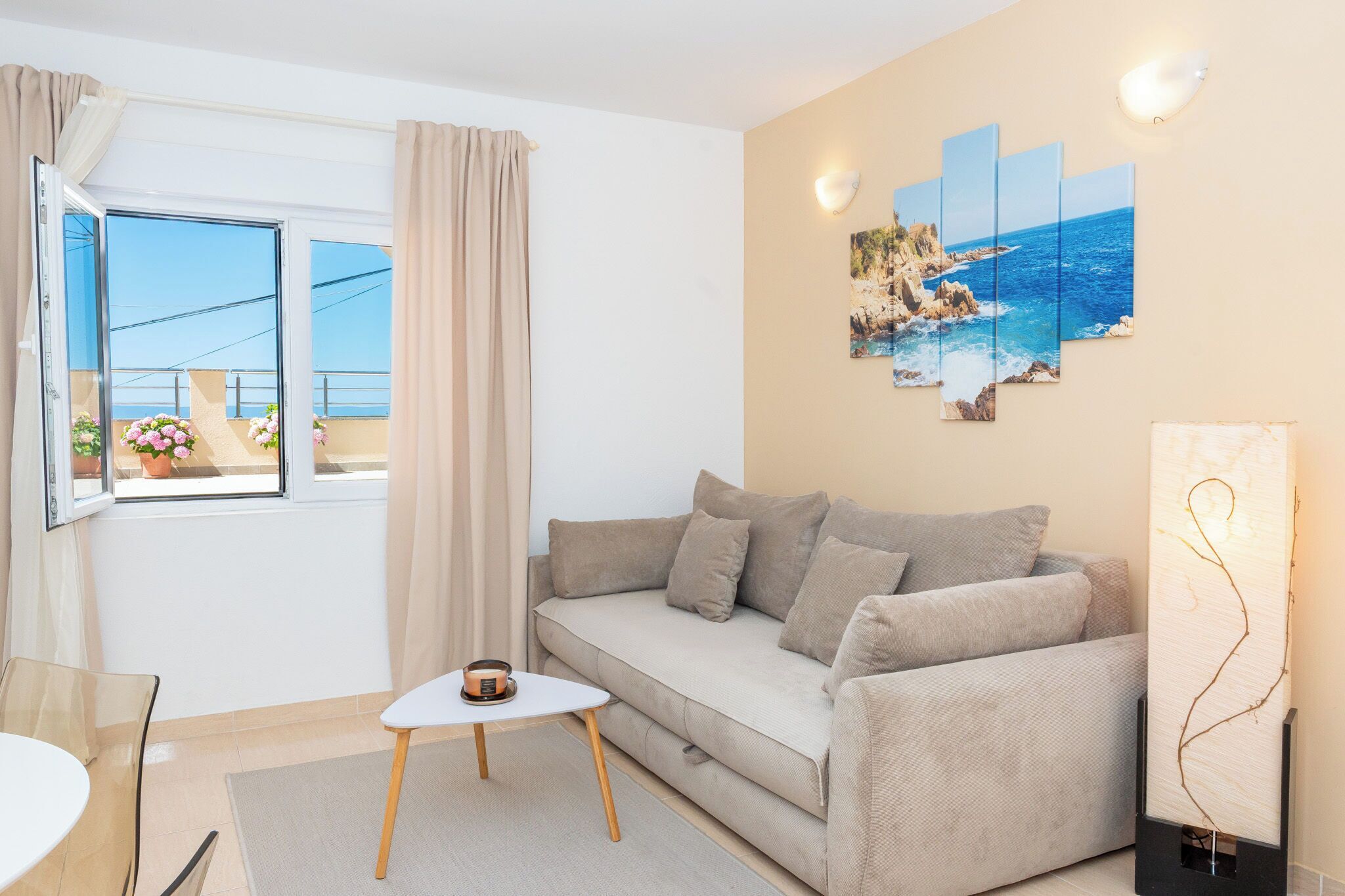 A modern living room with a sofa, a small table, a window with curtains, and a wall with a painting.