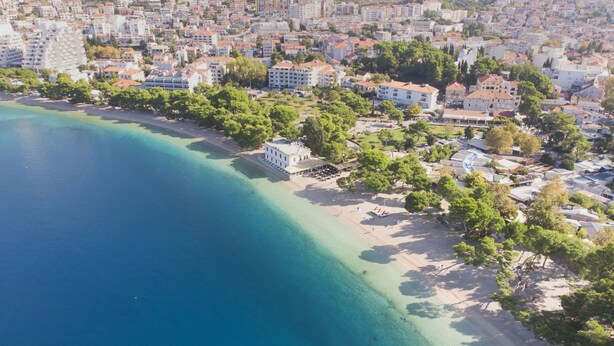 An aerial view of a coastal town with a beach, buildings, and greenery. - Apartments Pavlinovic (Makarska)