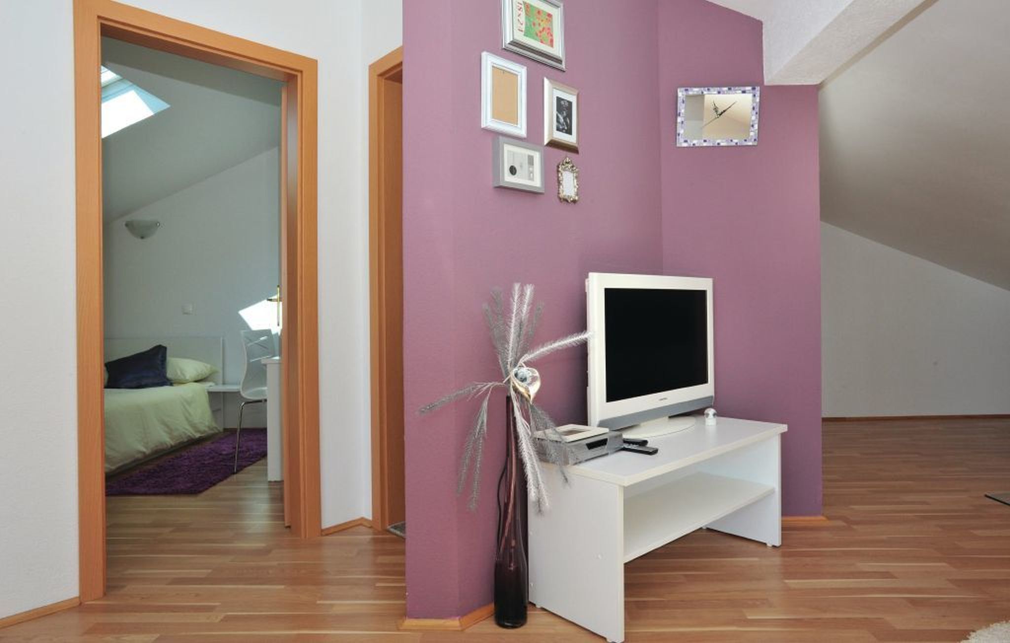 Ein Zimmer mit weißem Fernsehschrank, einem Flachbildfernseher und einer Wanduhr.
