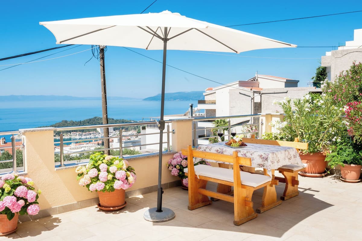 A balcony with a table and chairs, potted plants, and a view of the sea.