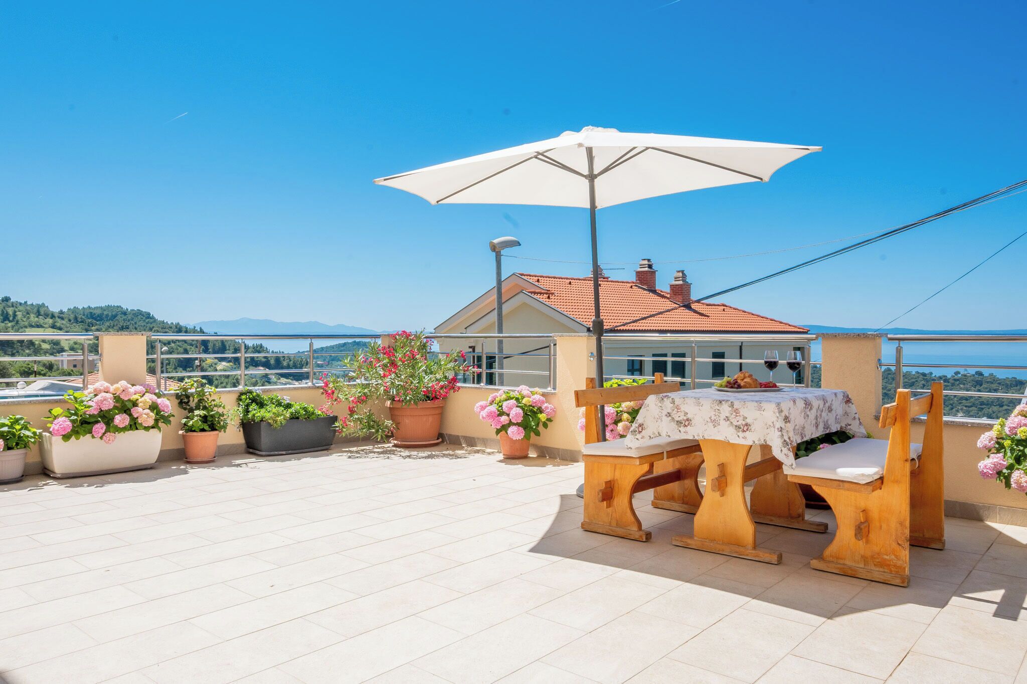 Una terrazza con tavolo e sedie, piante in vaso e vista sul mare.