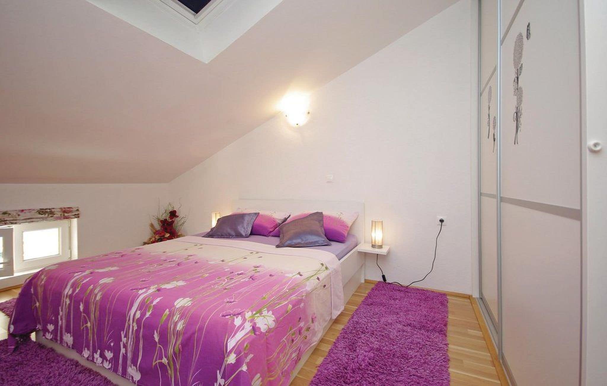 A bedroom with a bed, a nightstand, a wall-mounted light, and a window.