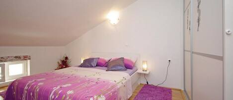 A bedroom with a bed, a nightstand, a wall-mounted light, and a window.