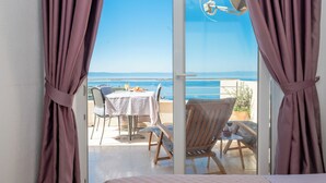 A balcony with a table and chairs, a view of the sea, and a window with curtains. - Apartments Pavlinovic (Makarska)