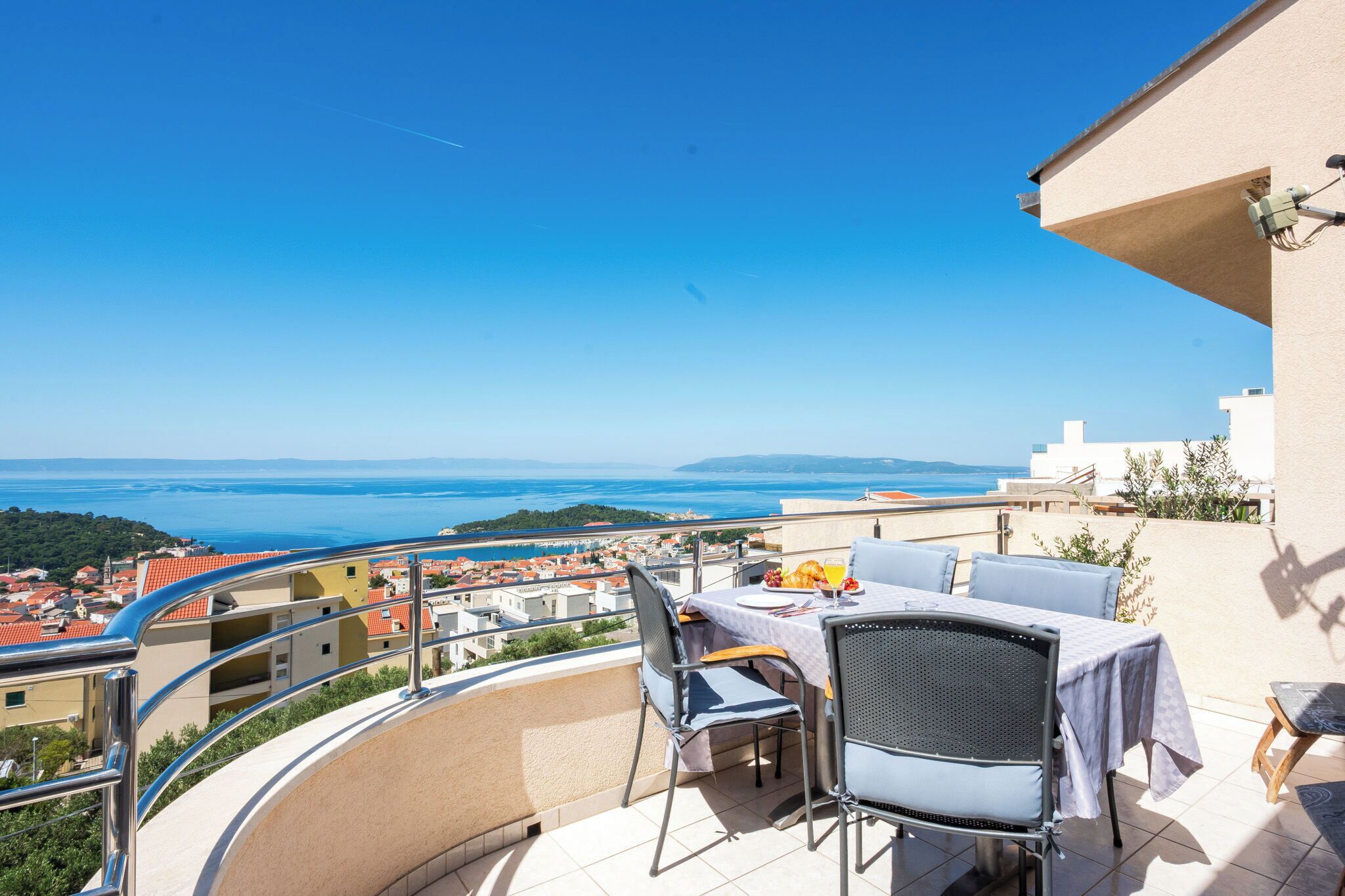 A balcony with a table and chairs, overlooking a coastal view.