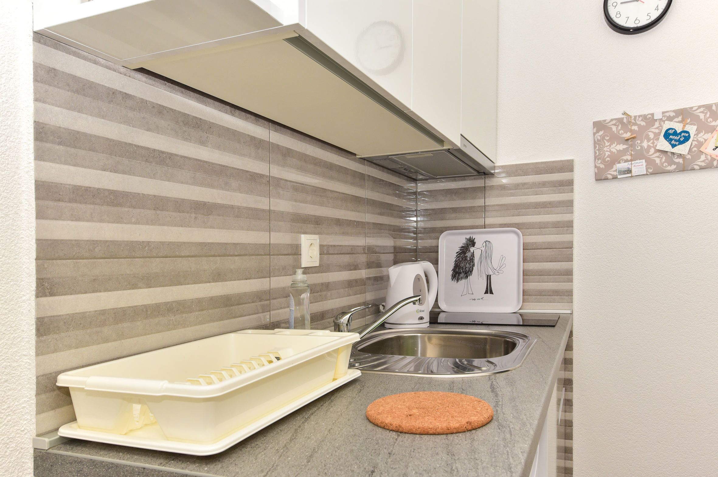 A kitchen with striped backsplash, stainless steel sink, and a kettle.