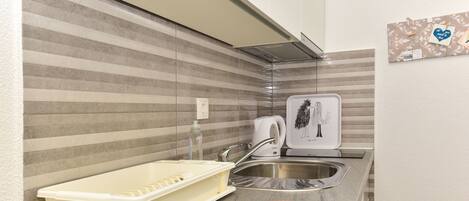 A kitchen with striped backsplash, stainless steel sink, and a kettle.