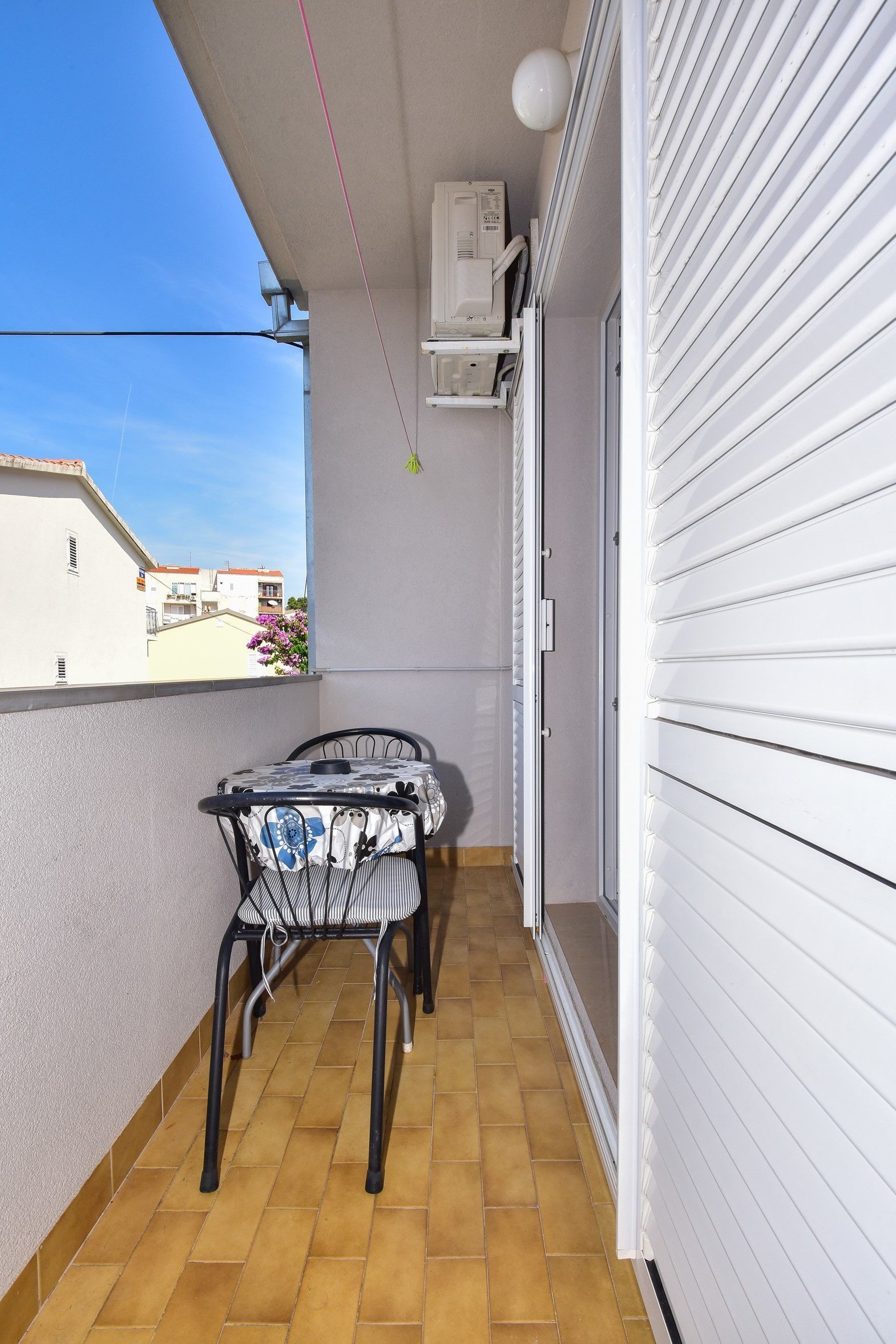 A balcony with a table and chairs, a sliding door, and an air conditioning unit.