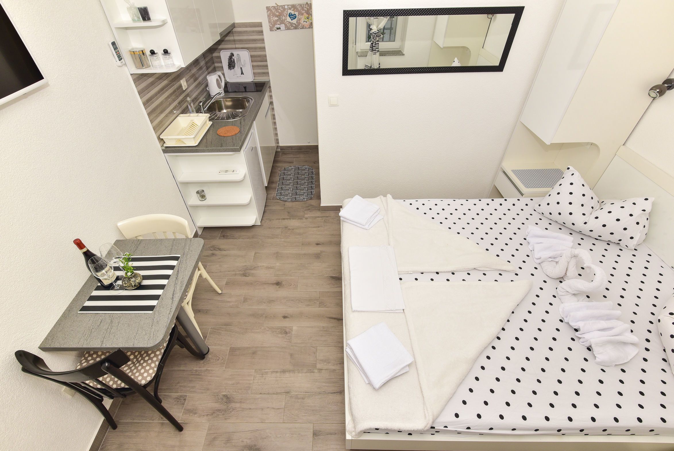Ein kleines Hotelzimmer mit Bett, einem Esstisch, einer Weinflasche und einer Küchenzeile.