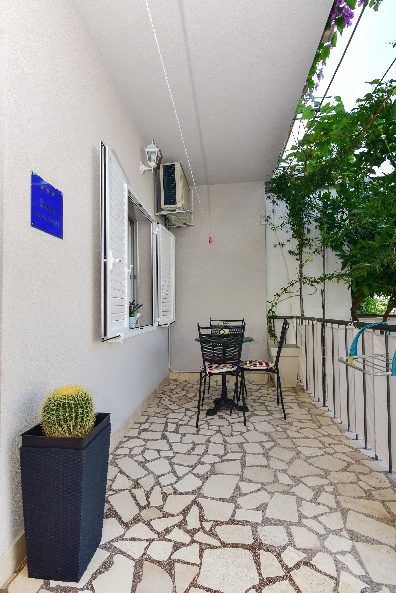 A balcony with a tiled floor, a table with chairs, a potted cactus, and a blue sign on the wall.