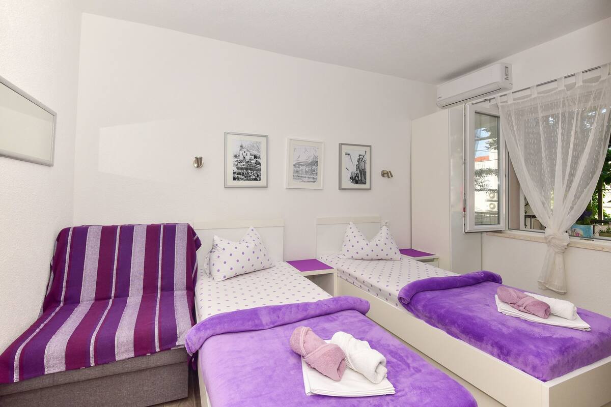 Une chambre d’hôtel avec deux lits simples, un canapé et une fenêtre avec des rideaux légers.