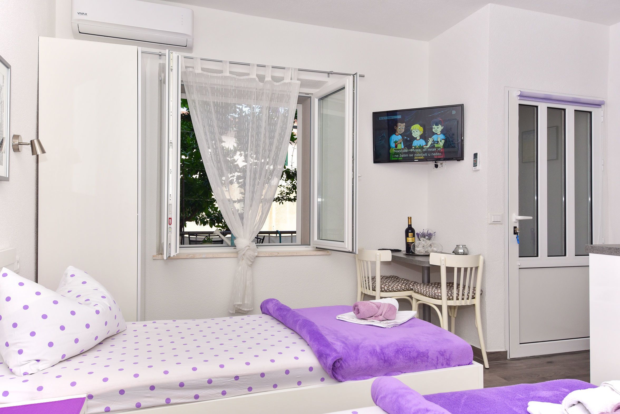 Un dormitorio con cama, televisor, ventana con cortina y una silla.