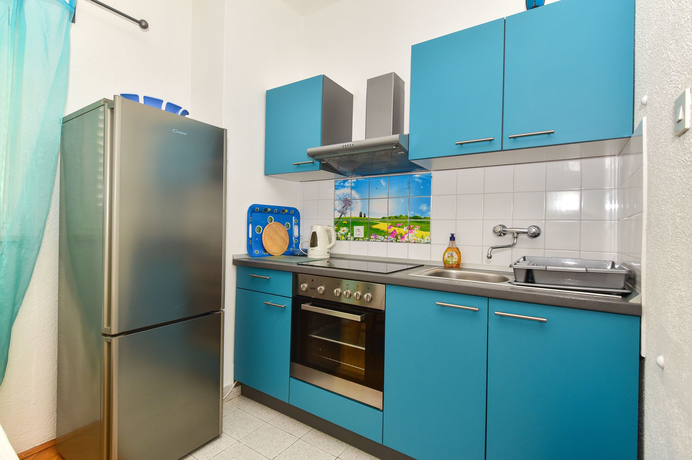 Una cocina con armarios azules, un refrigerador de acero inoxidable, una estufa y un lavamanos.