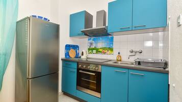 Una cocina con armarios azules, un refrigerador de acero inoxidable, una estufa y un lavamanos.