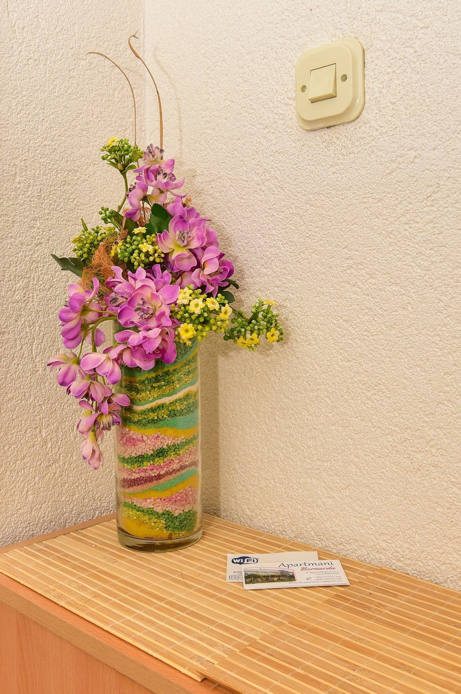 A vase with flowers on a wooden surface against a textured wall.
