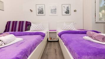 Une chambre double avec deux lits, une literie violette et une petite table de chevet sur laquelle se trouve un livre.