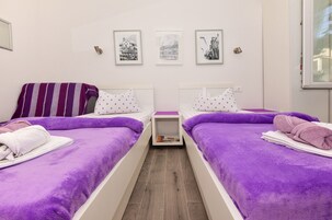 A twin room with two beds, purple bedding, and a small bedside table with a book.