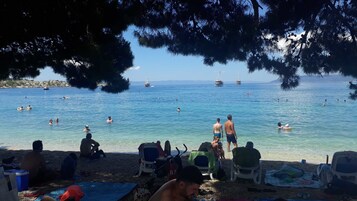 En strand med klart, blåt vand, folk der svømmer og solbader, og både i det fjerne.