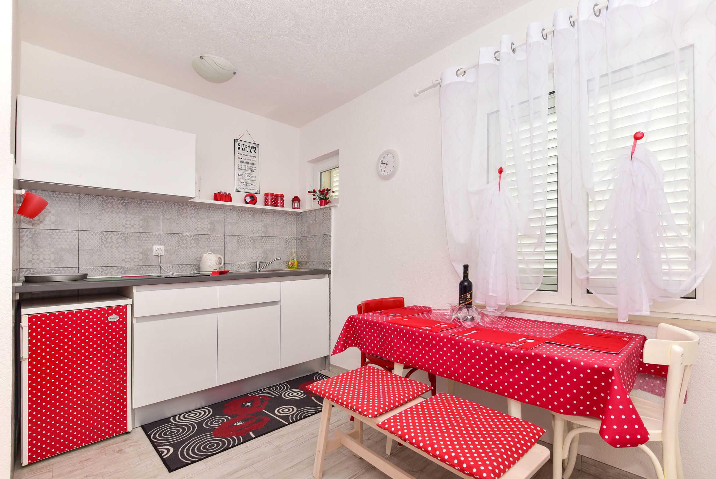 A compact kitchen with white cabinets, a red refrigerator, and a dining area with a red tablecloth and matching chairs.