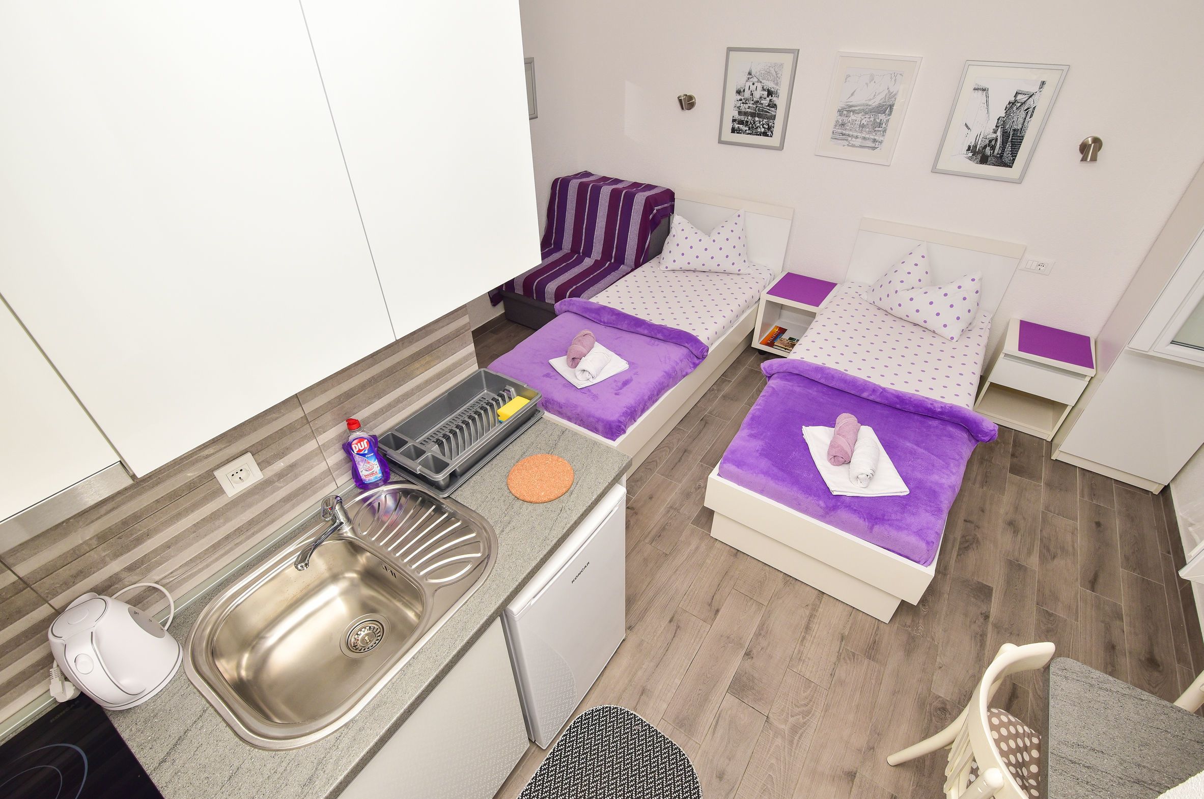 Ein kompaktes Hotelzimmer mit zwei Betten, einer Küchenzeile und einem kleinen Badezimmer.