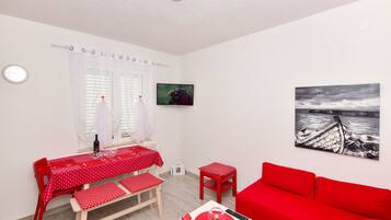A room with a red table and chairs, a red sofa, a painting of a boat, and a window with curtains.