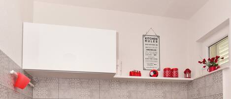 Una cocina con armarios blancos, un refrigerador rojo con lunares, un tapete negro con flores rojas y un cartel que dice 'Kitchen Rules'.