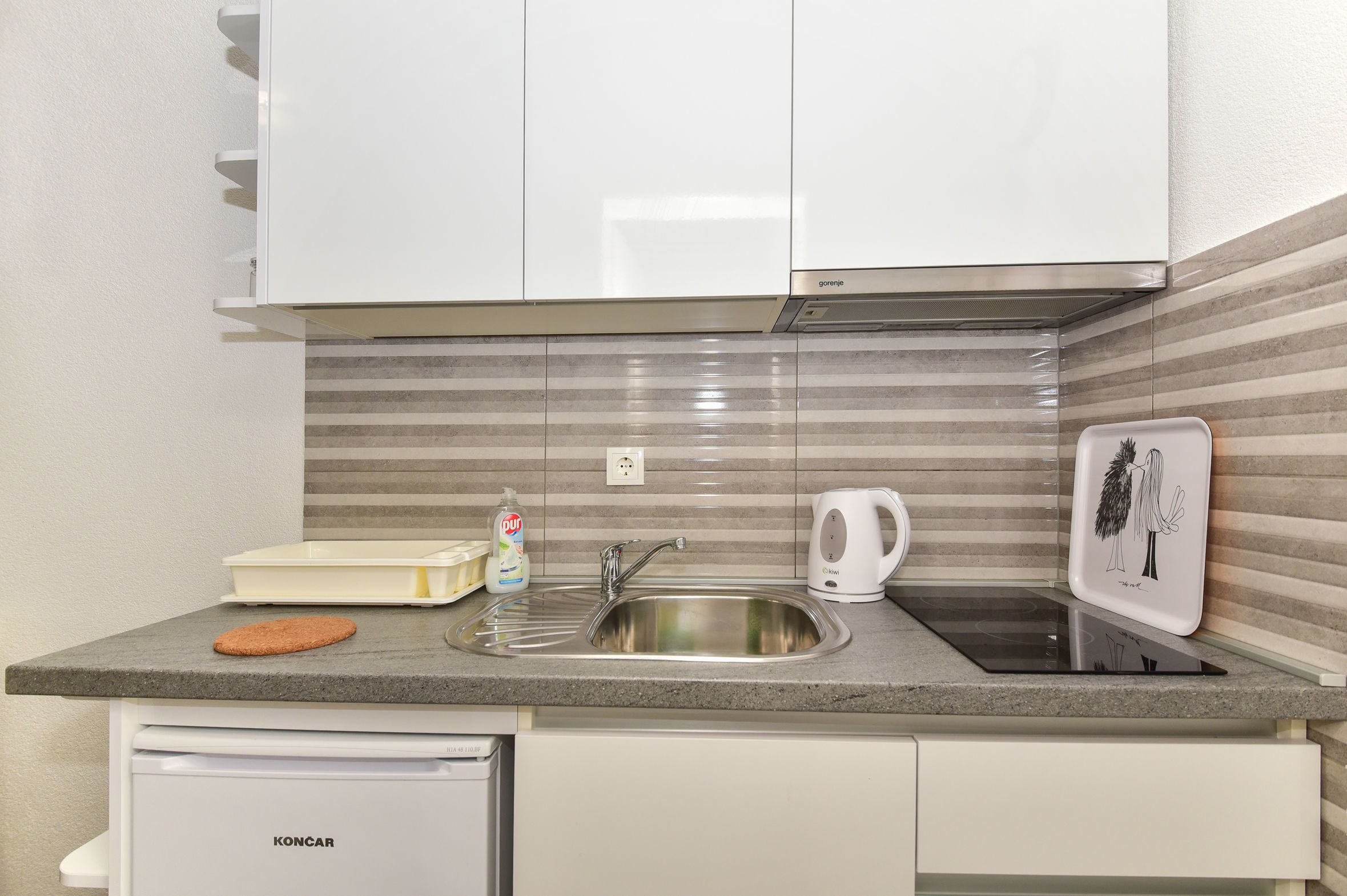 Cocina compacta con un lavamanos de acero inoxidable, hervidor y tostadora.