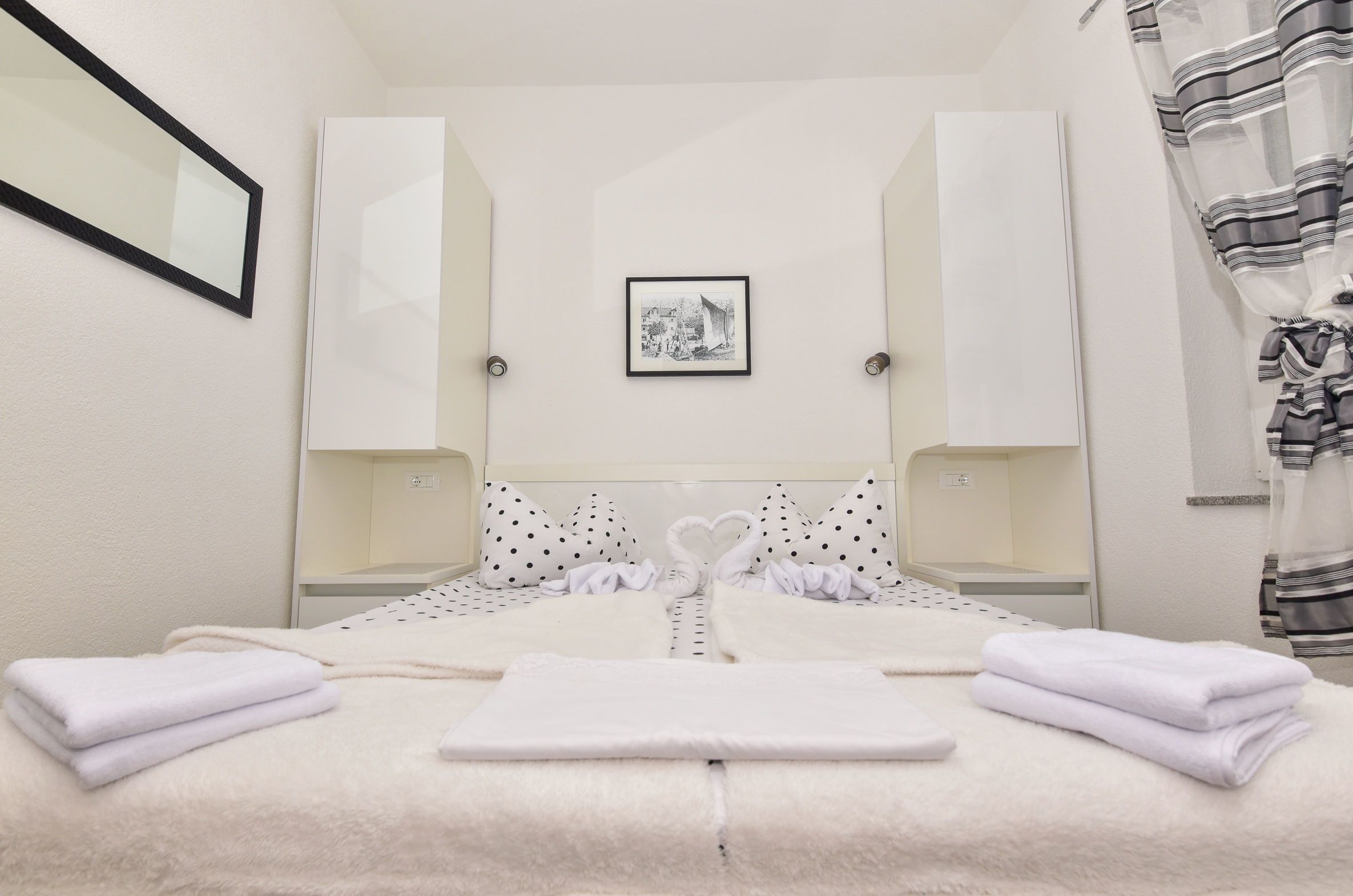 Een netjes opgemaakt bed met witte handdoeken, een decoratieve handdoek in de vorm van een hart, en een lijst met een foto aan de muur.
