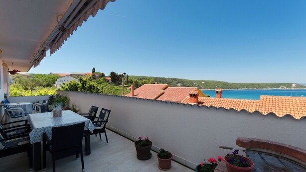A terrace with a table and chairs, potted plants, and a view of the sea and hills. - Apartment Anica (Kampor)