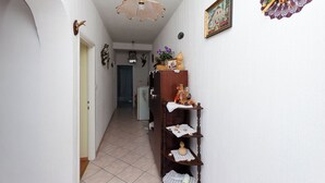A hallway with a white door, a wooden shelf with decorative items, a hanging light fixture, and a framed picture on the wall. - Apartment Anica (Kampor)