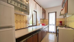 A kitchen with wooden cabinets, a white refrigerator, and a window with curtains. - Apartments Luka (Mali Losinj)