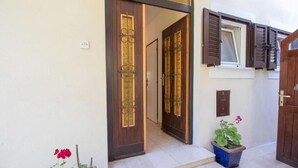 A building entrance with a wooden door, a window with shutters, and a potted plant. - Apartments Luka (Mali Losinj)
