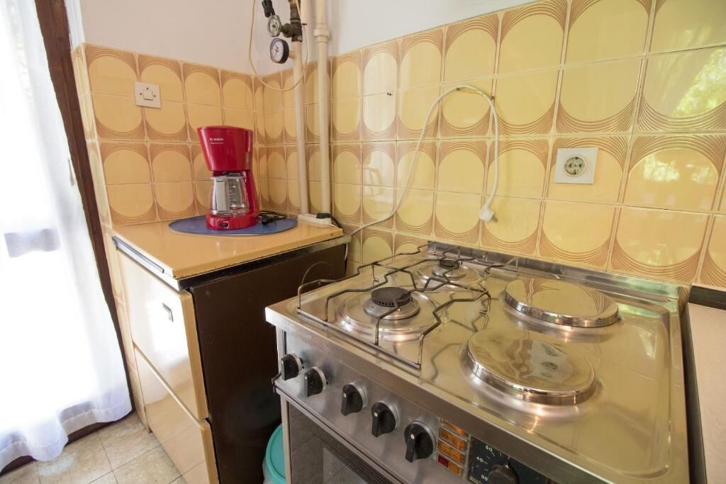 Cuina amb fogó de gas, cafetera vermella i respold de rajoles amb dibuixos.