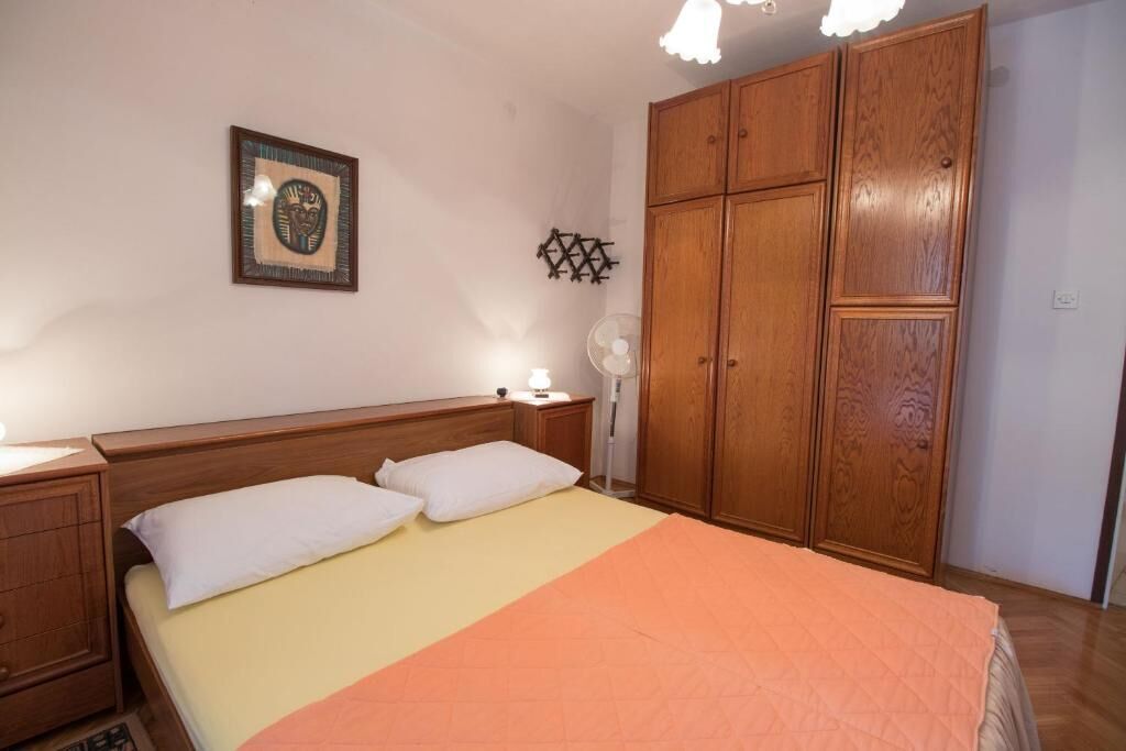 A bedroom with a bed, wooden wardrobe, bedside table, and a wall-mounted decorative item.