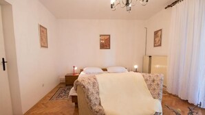 A bedroom with a bed, bedside lamps, a nightstand, a floral chair, and a wooden floor. - Apartments Luka (Mali Losinj)