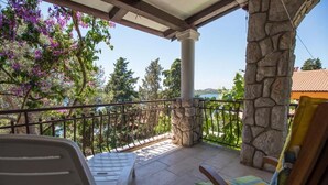 A covered outdoor seating area with stone pillars, a view of the surrounding landscape, and a railing. - Apartments Luka (Mali Losinj)