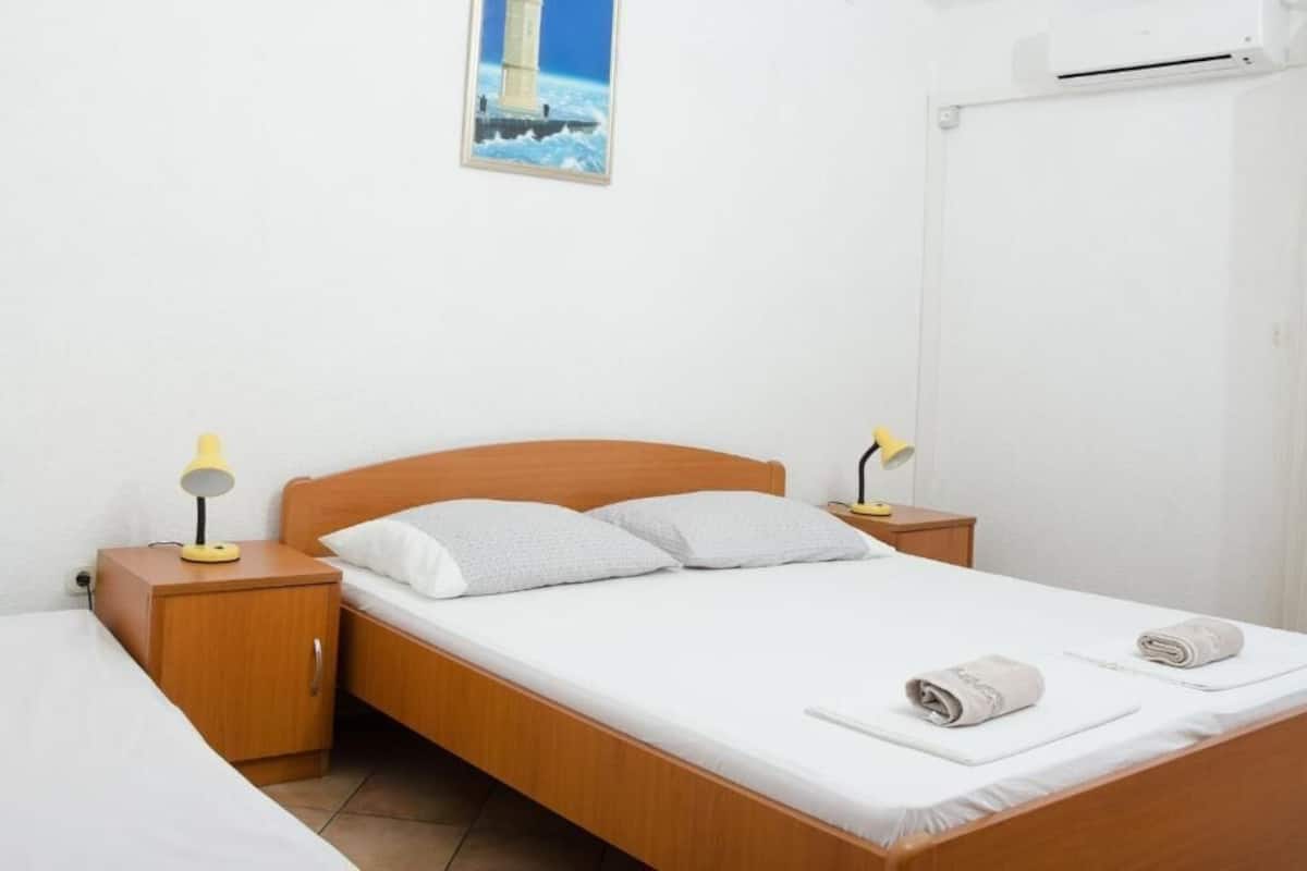 A single bed with a wooden headboard, two bedside tables with lamps, a white wall, and a framed picture of a lighthouse.