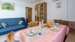 A dining area with a table set for four, a blue sofa, a wooden cabinet, and a painting on the wall. - Apartments Bozana (Dramalj)