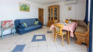 A living room with a blue sofa, a dining table with a pink tablecloth, and a wooden cabinet. - Apartments Bozana (Dramalj)