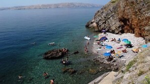 A rocky beach with clear water, people swimming and sunbathing, and umbrellas.
