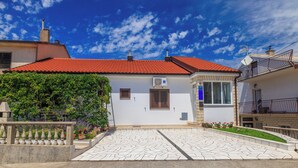A two-story house with a red-tiled roof, white walls, and a stone-paved courtyard.