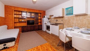 A compact kitchen with wooden cabinets, a dining table set for four, and a sofa in the living area.