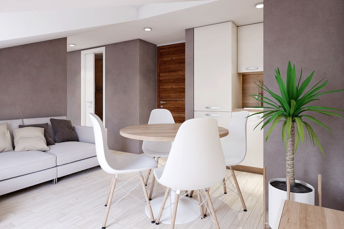 A modern living room with a sofa, white chairs, a round table, and a potted plant.